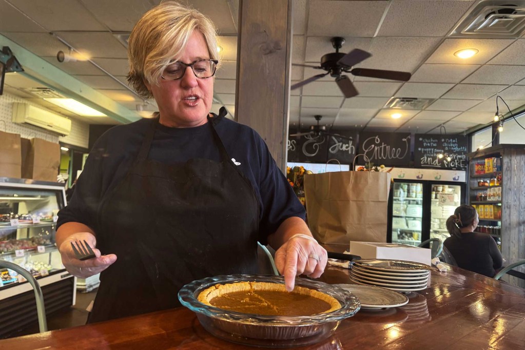 A woman wearing an apron checking out a pie at a counter inside a restaurant.