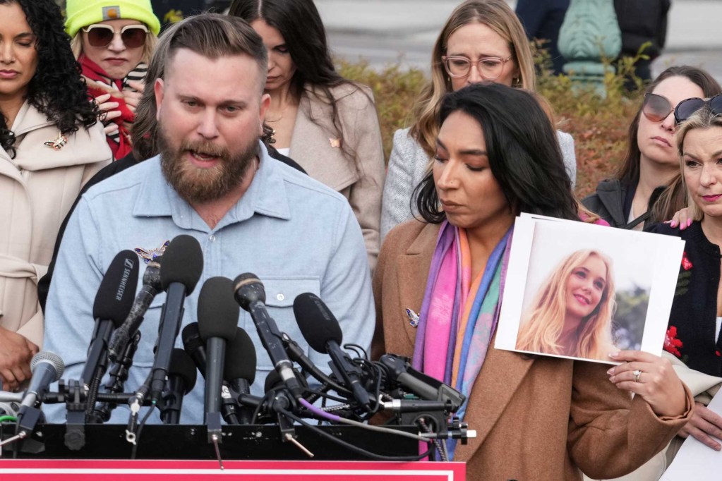 Sky Roberts speaks at a press conference as someone holds up a photo of his sister Virginia Giuffre beside him